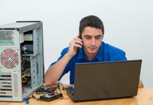 Un dépanneur informatique en chemise bleue diagnostique une panne sur un ordinateur portable tout en étant au téléphone