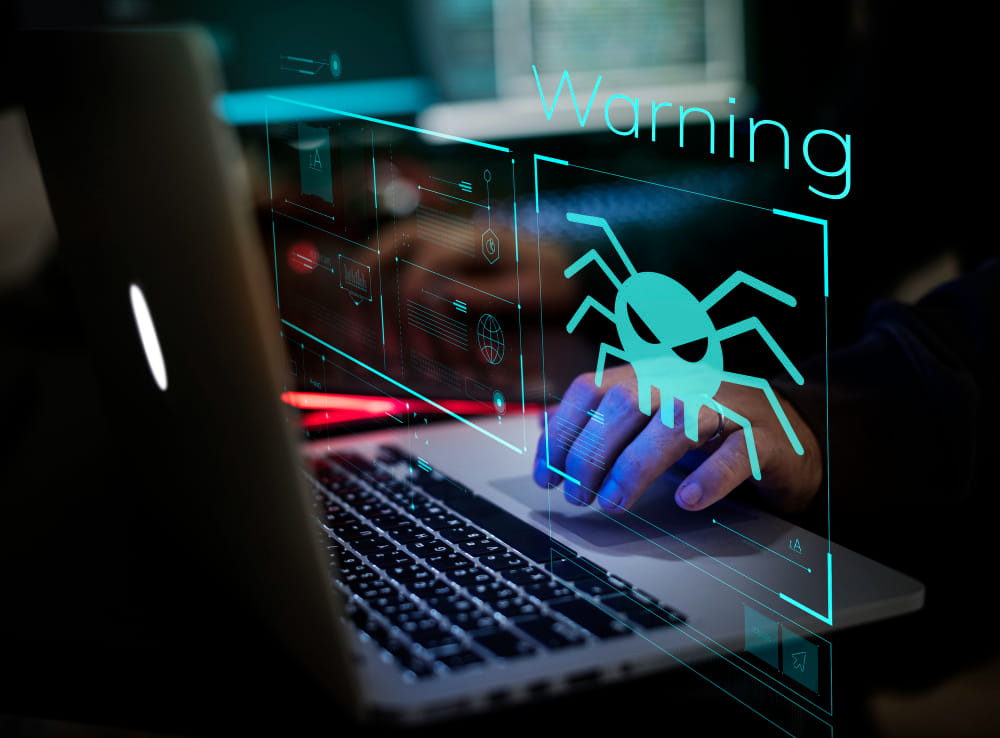 Une main s'apprête à cliquer sur un ordinateur portable affichant une alerte de sécurité numérique "Warning" et une icône d'araignée malveillante, nécessitant l'intervention d'un dépanneur informatique